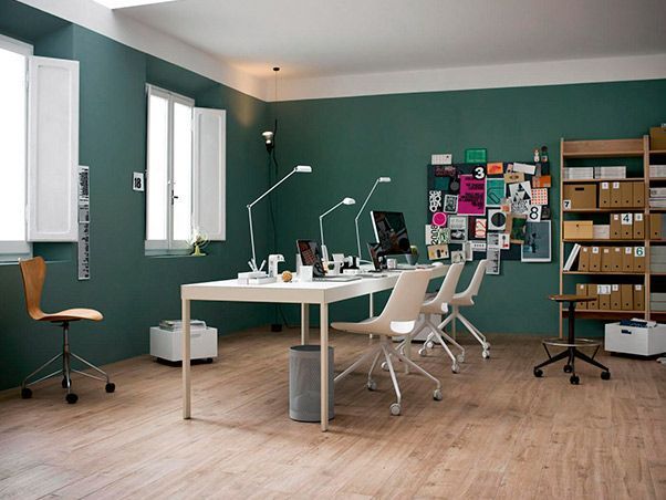 Una habitación con paredes verdes y pisos de madera tiene un escritorio y sillas.