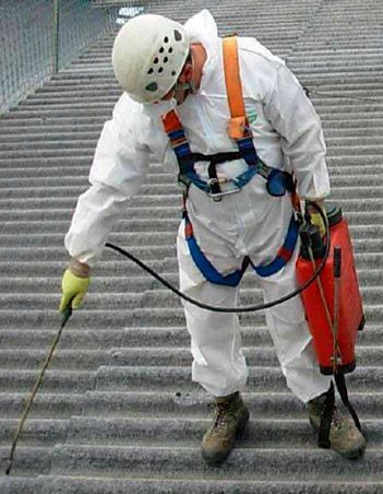 Un hombre con un traje blanco está rociando algo en un techo.