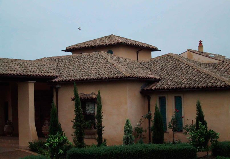 Una casa grande con techo de tejas está rodeada de árboles y arbustos.