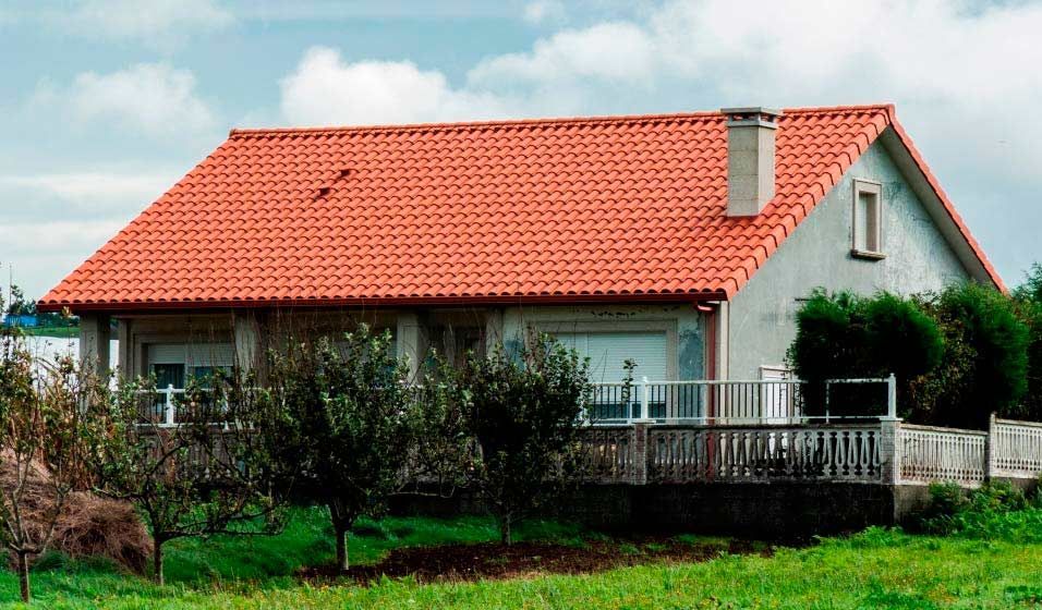 Una casa con techo de tejas rojas está en medio de un campo de hierba.