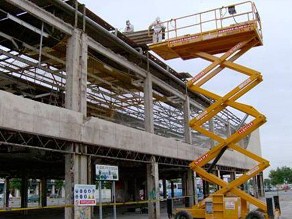 Un hombre está parado en un elevador de tijera frente a un edificio en construcción.