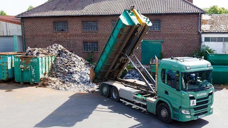 Ein grüner Muldenkipper steht vor einem Backsteingebäude.