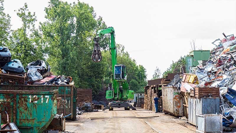 Ein grüner Kran bewegt einen Haufen Altmetall auf einem Schrottplatz.