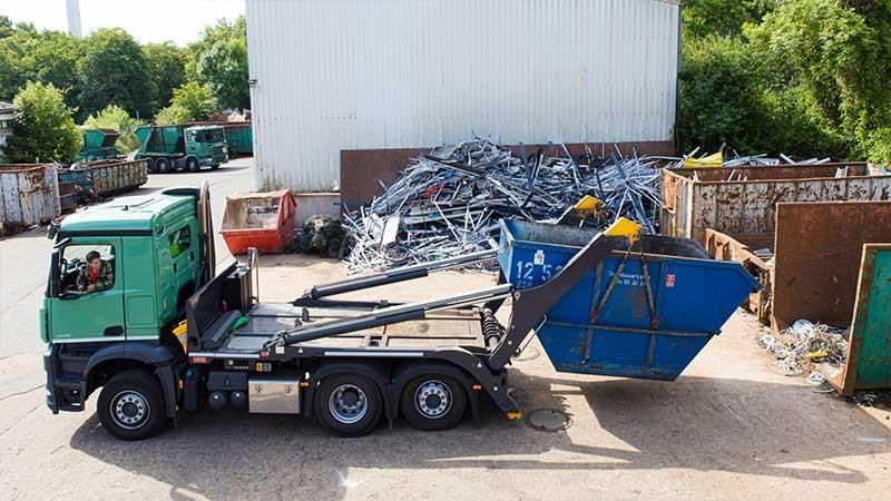 Ein grüner Muldenkipper mit einem daran befestigten blauen Müllcontainer