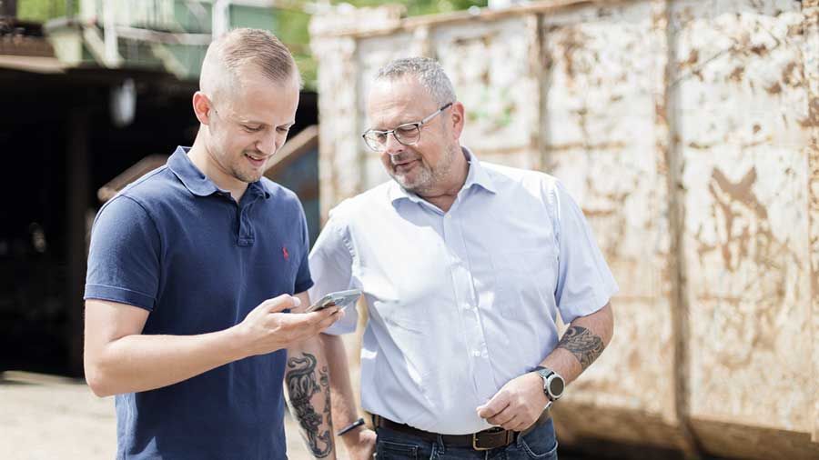 Zwei Männer stehen nebeneinander und schauen auf ein Mobiltelefon.