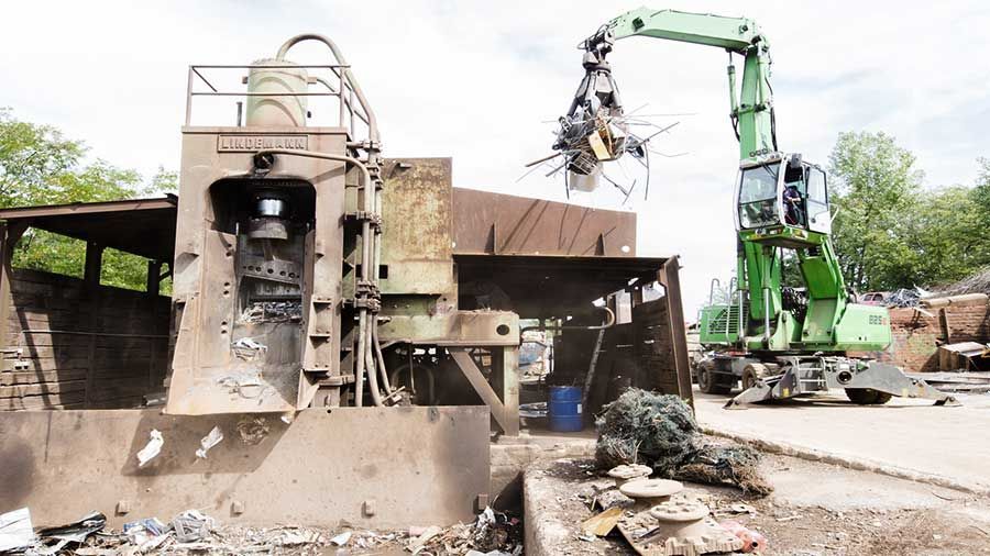 Ein grüner Kran hebt ein Stück Metall auf einem Schrottplatz