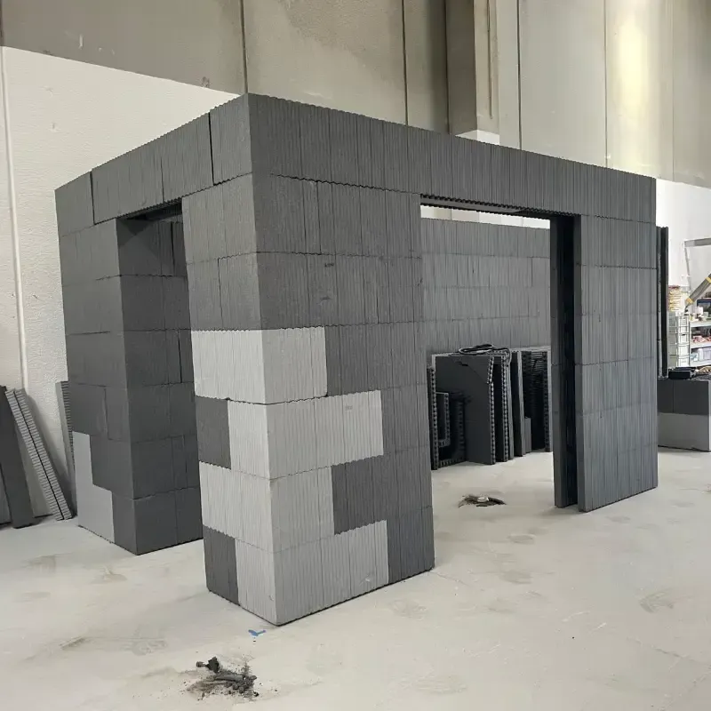 Estructura de bloques grises en construcción en un taller, con paneles rectangulares apilados y una puerta abierta.