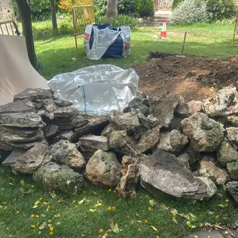 Pila de rocas grandes en un jardín, junto a una lona y una zona de excavación de tierra.
