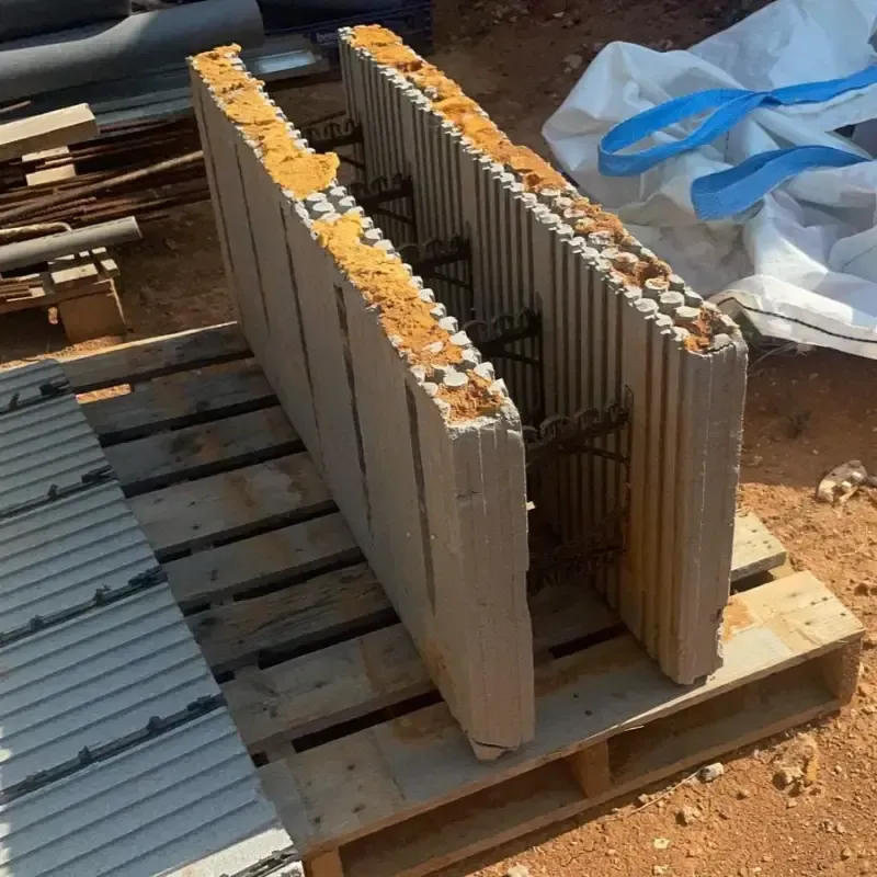 Losas de hormigón gris apiladas sobre palés de madera al aire libre, con correas de plástico azules cerca.