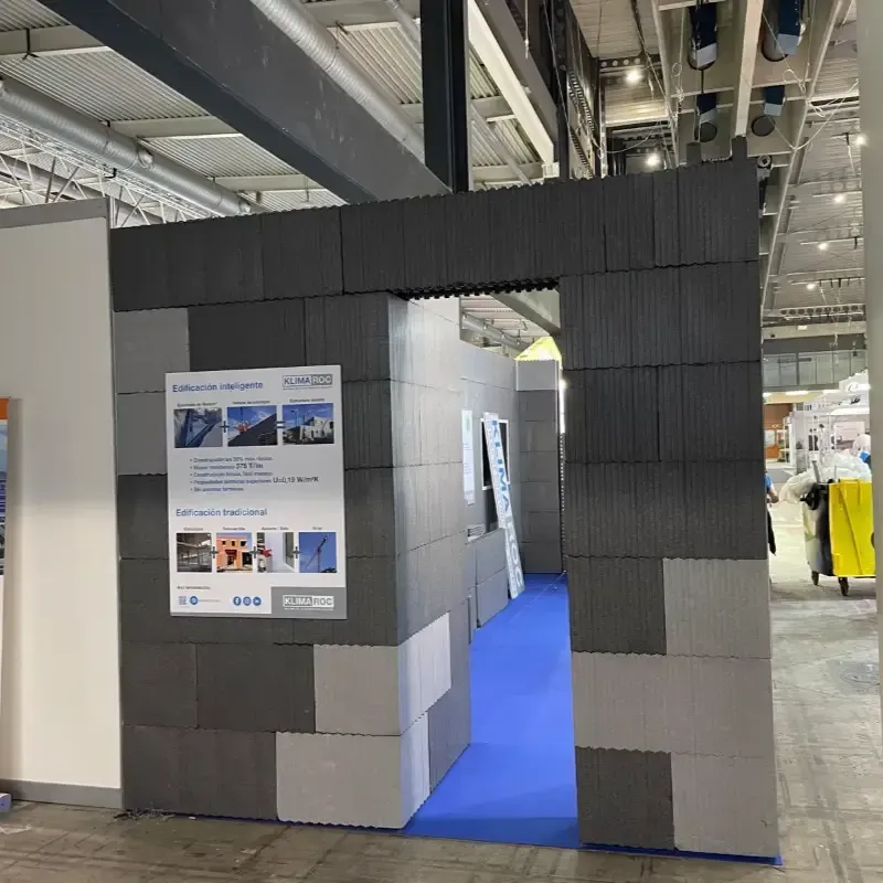 Entrada a un stand de exposición con paneles gris oscuro y alfombra azul en un recinto ferial.