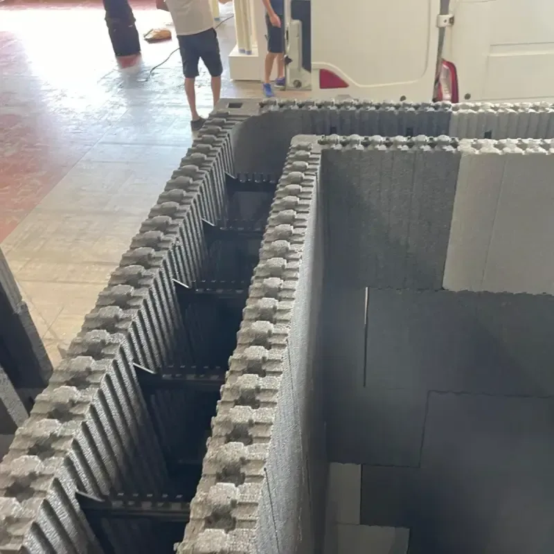 Zanja de bloques de hormigón con agua oscura o un vacío en su interior, ubicada en una zona de construcción o exposición.