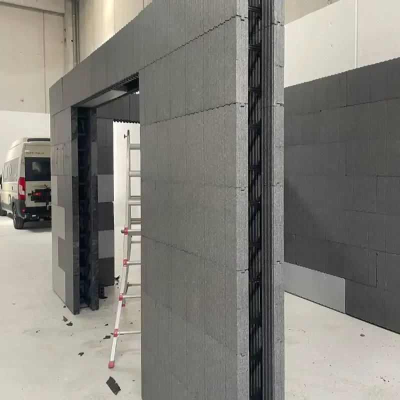 Obra en construcción en el interior de una habitación blanca, con paredes de bloques grises, una furgoneta y andamios.