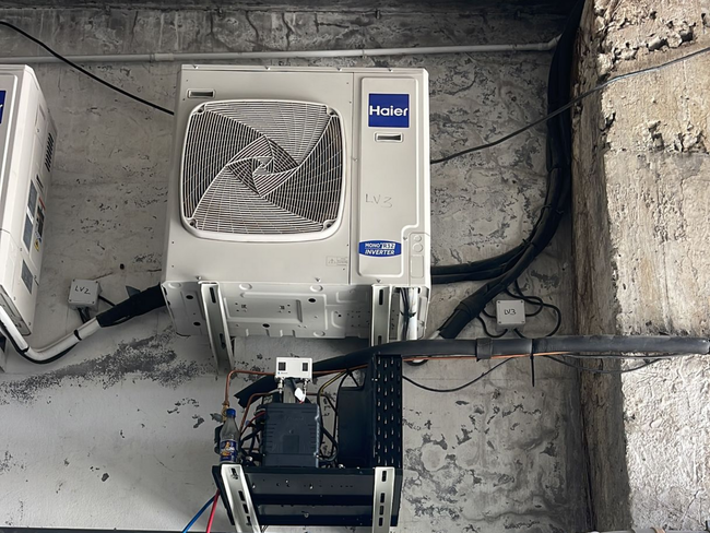Un technicien portant des gants de travail installe un climatiseur sur un mur extérieur blanc.