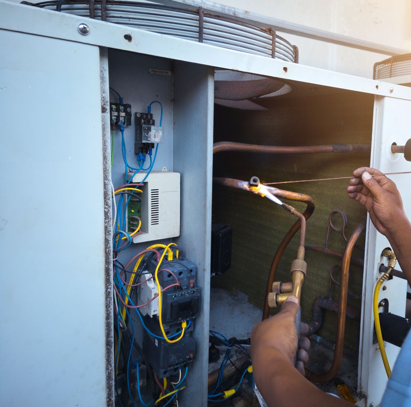 Un technicien utilise un chalumeau à l'intérieur de l'armoire d'une unité de climatisation industrielle.