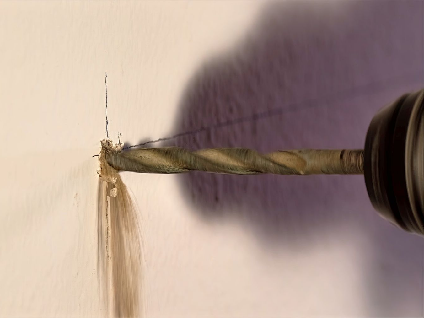 Une mèche de perceuse perçant un mur blanc.