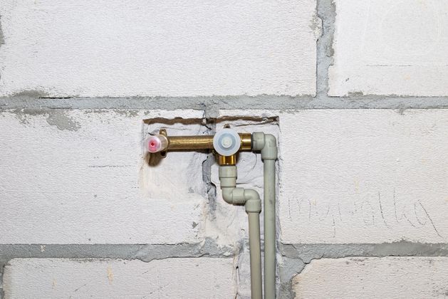 Un raccord de plomberie en laiton avec deux tuyaux gris clair, installé contre un mur.
