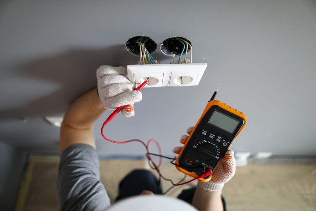 Un électricien portant des gants utilise un multimètre pour tester une prise électrique.