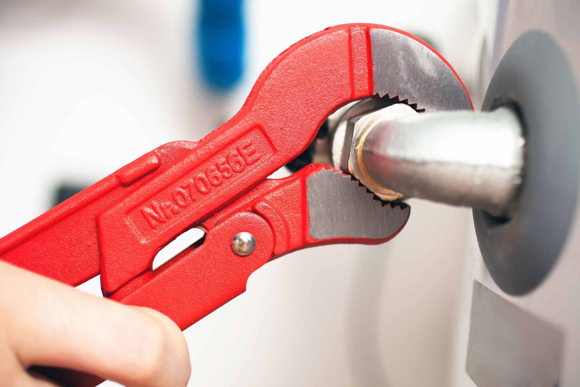 Une main utilise une clé à pipe rouge pour serrer un raccord de tuyau métallique sur un chauffe-eau.