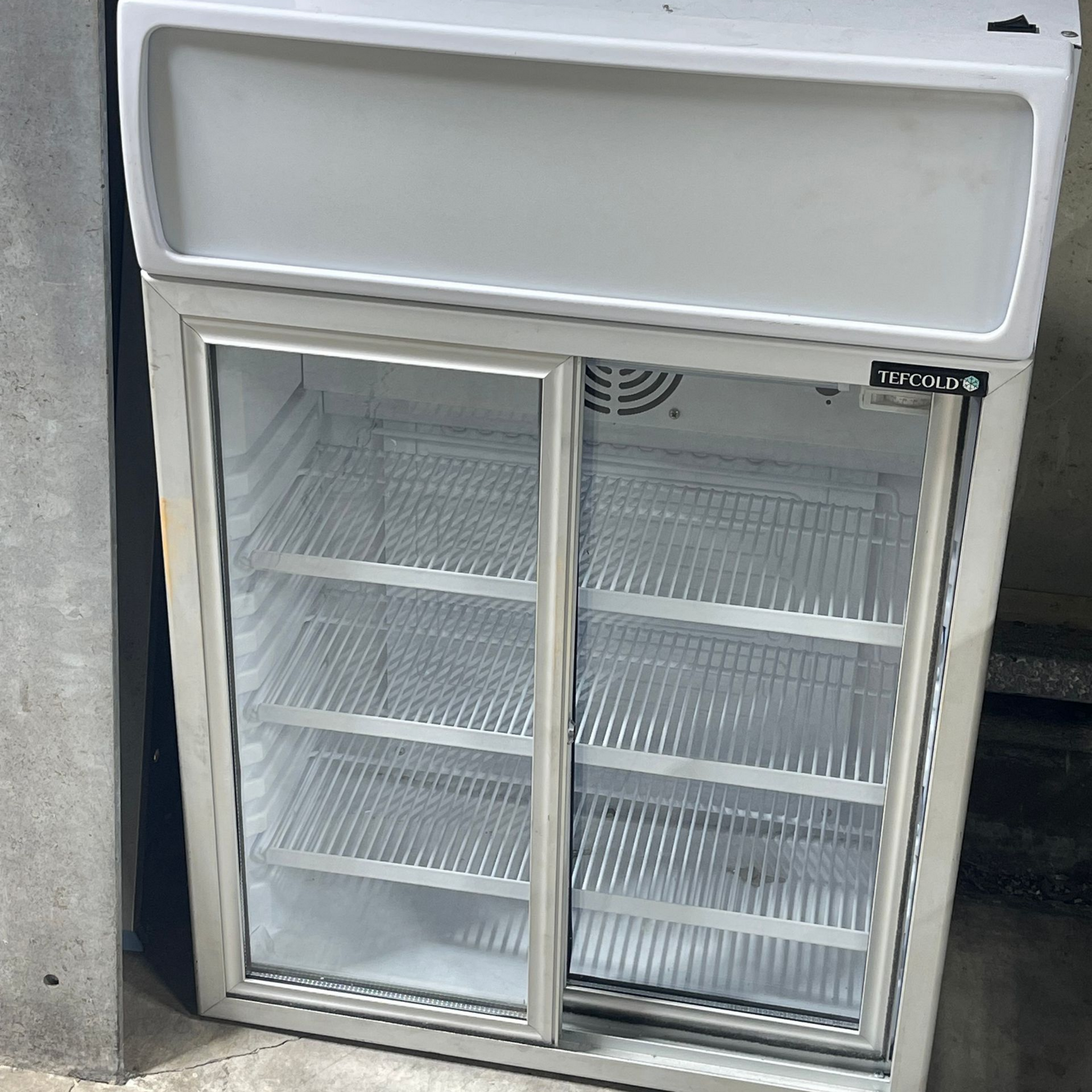 Un boulanger transporte un plateau de pains vers un réfrigérateur industriel ouvert rempli de produits de boulangerie.