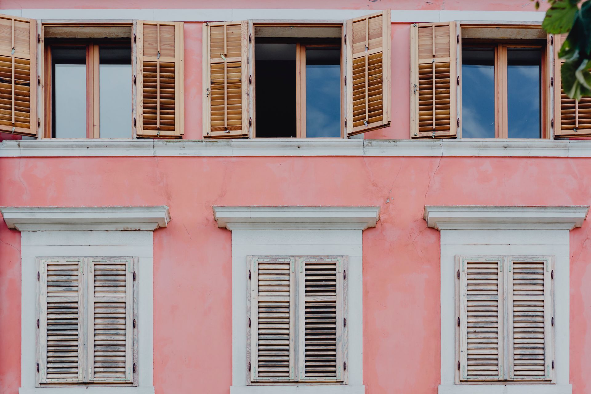 Edificio rosa con ventanas abiertas, contraventanas de madera y marcos blancos.