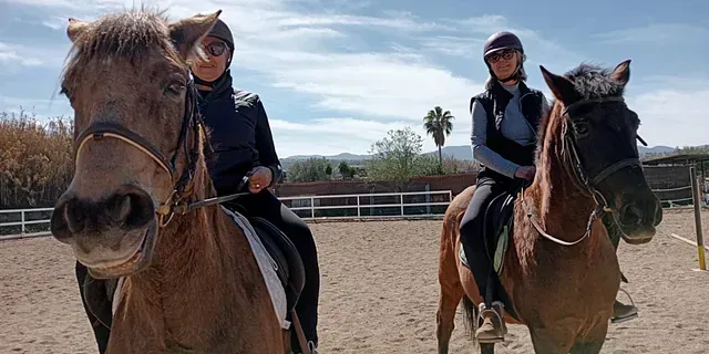 Dos personas montan a caballo en una pista de tierra.