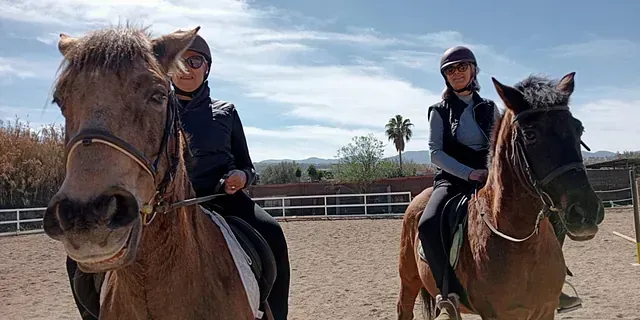 Dos personas montan a caballo en una zona vallada.