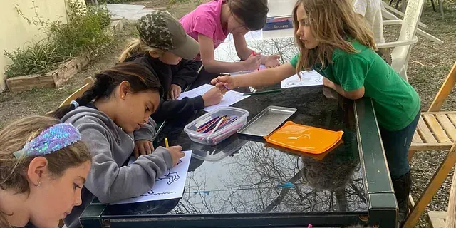 Un grupo de chicas jóvenes están sentadas en una mesa dibujando.