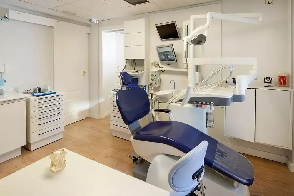 Consultorio dental moderno con sillón azul, equipo, gabinetes y lavabo.