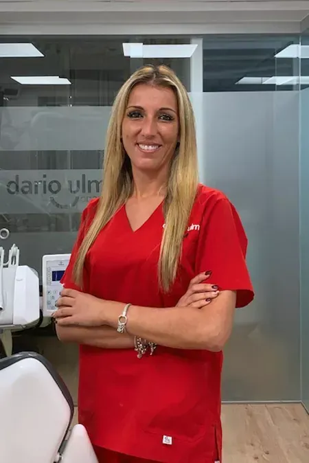 Mujer con camisa roja de pie en una oficina con los brazos cruzados y sonriendo.