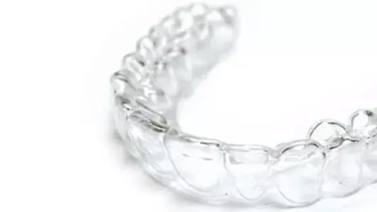 Una férula de alineador dental transparente de plástico, mostrada sobre un fondo blanco.
