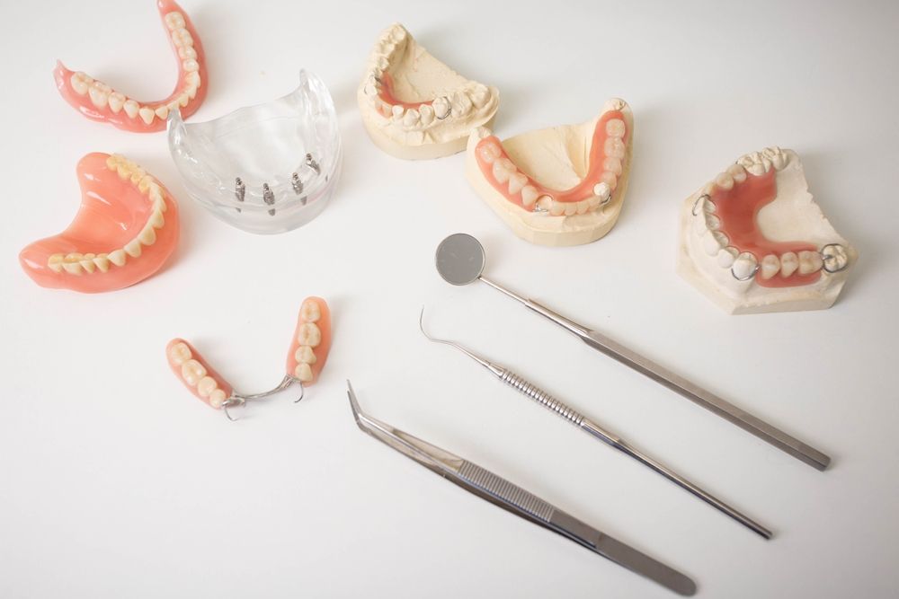 Una colección de prótesis dentales, que incluye varias dentaduras postizas y moldes, expuestas junto con instrumental dental sobre una superficie blanca.