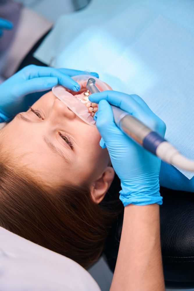 Un dentista con guantes médicos azules utiliza una pieza de mano para realizar un procedimiento en un paciente que lleva un separador de mejillas.