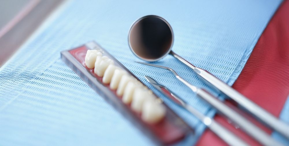Espejo dental, explorador y una hilera de dientes artificiales en una bandeja cubierta con un babero azul.