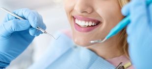 Un paciente sonríe mientras recibe un examen dental con instrumental profesional y guantes azules.