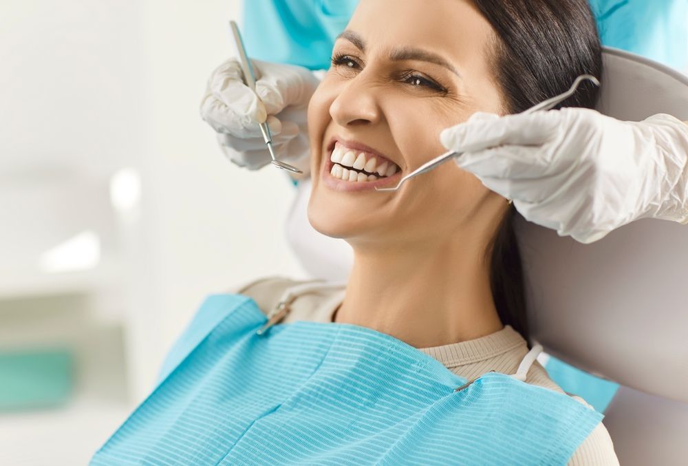 Una persona sonríe mientras le realizan un examen dental, con las manos enguantadas del profesional sosteniendo instrumentos cerca de su boca.