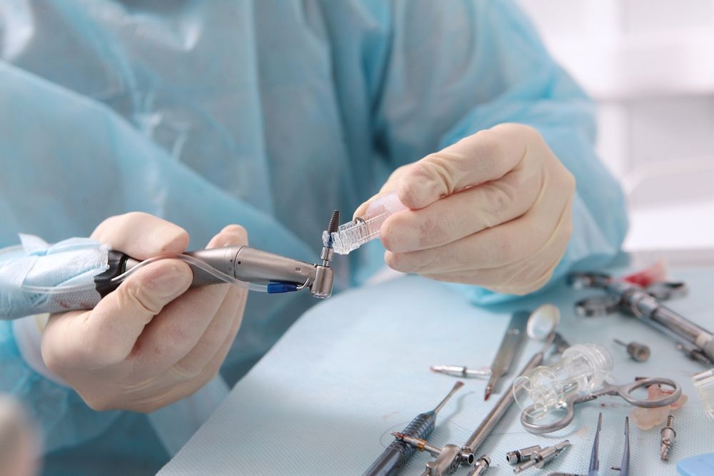 Un profesional dental, con guantes y bata azul, acopla una fresa a una pieza de mano dental en un entorno clínico.