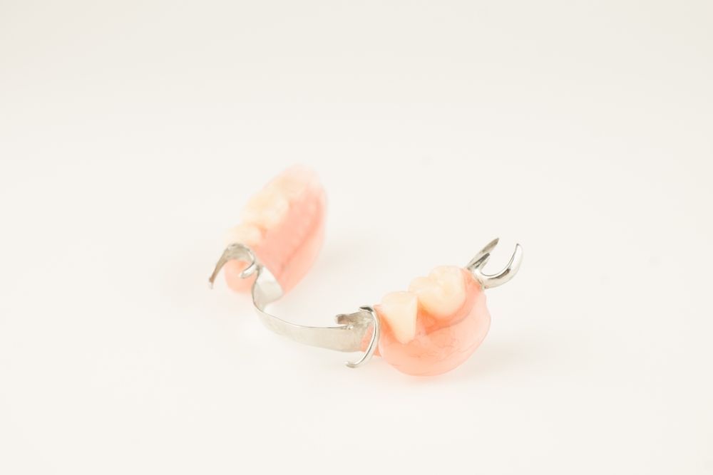 Una prótesis parcial dental que consta de dos segmentos de color rosa encía con dientes artificiales, conectados por una fina estructura metálica.