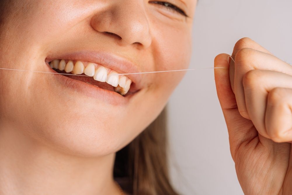 Una persona sonriendo mientras se pasa hilo dental sobre un fondo liso de color claro.