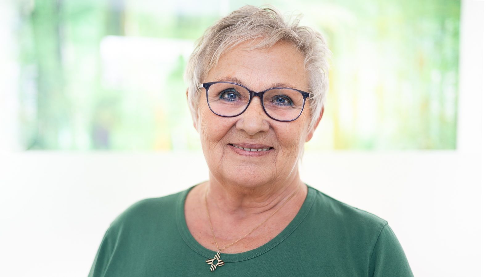 Eine Frau mit Brille und braunem Kasack lächelt in die Kamera.