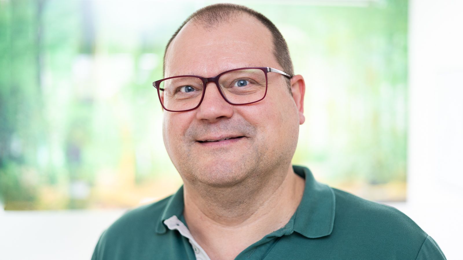 Ein Mann mit Brille und braunem Hemd lächelt in die Kamera.