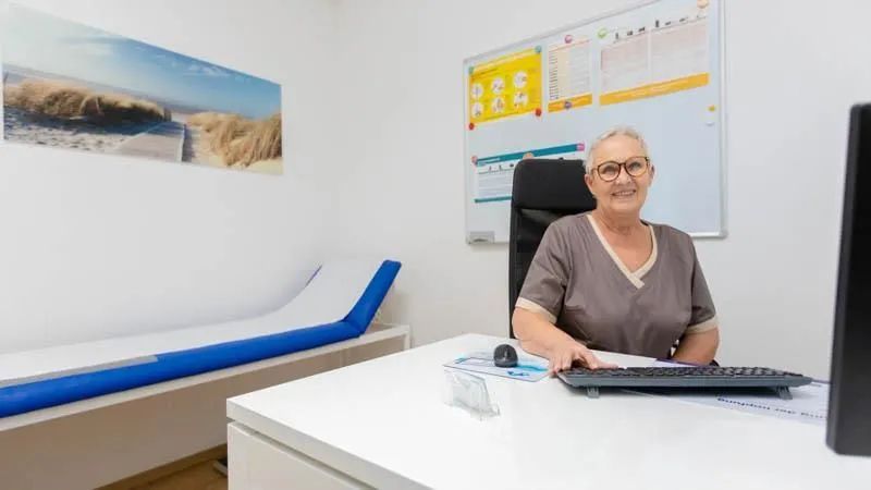 Eine Frau sitzt an einem Schreibtisch in einer Arztpraxis.