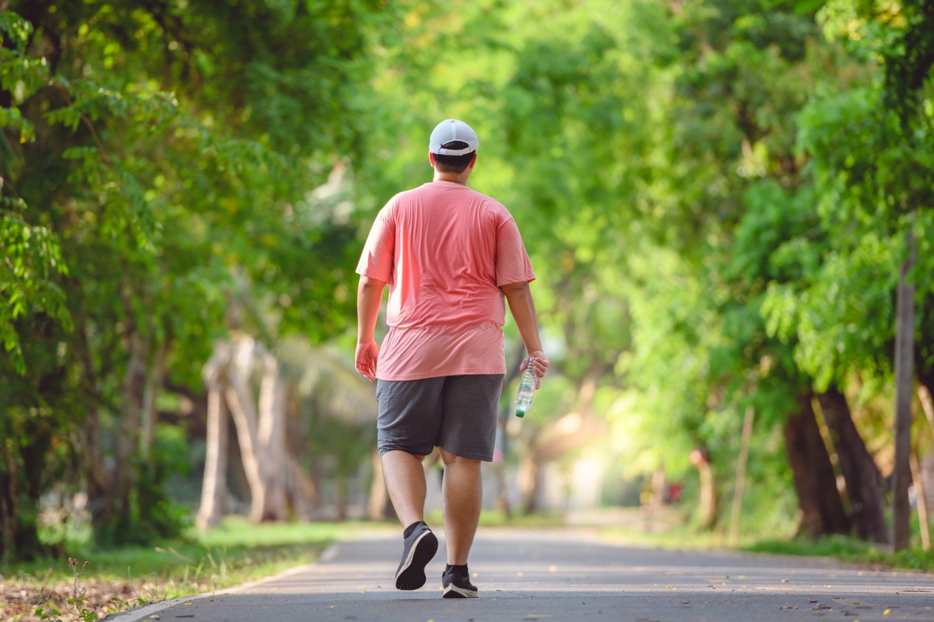 Ein Mann geht mit einer Flasche Wasser in der Hand einen Weg in einem Park entlang.