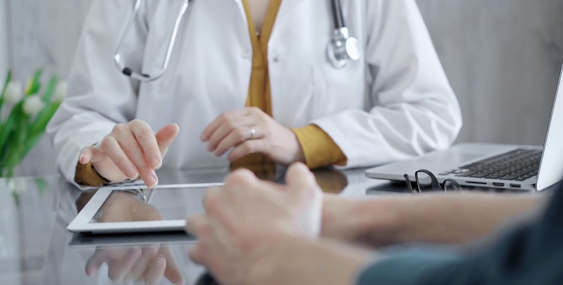Ein Arzt spricht mit einem Patienten und benutzt dabei einen Tablet-Computer.
