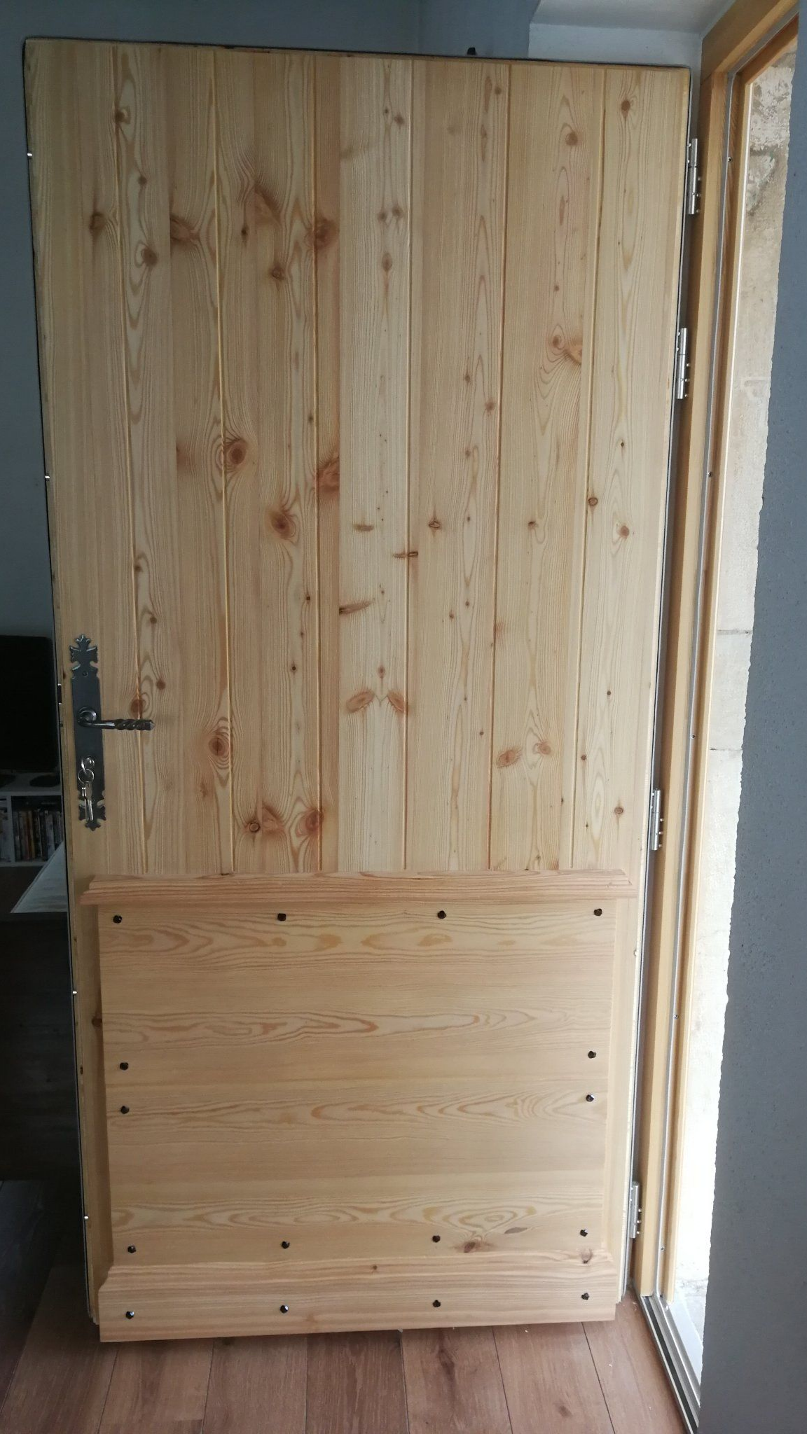 Porte en bois brut, à panneaux verticaux en partie supérieure et horizontaux en partie inférieure.