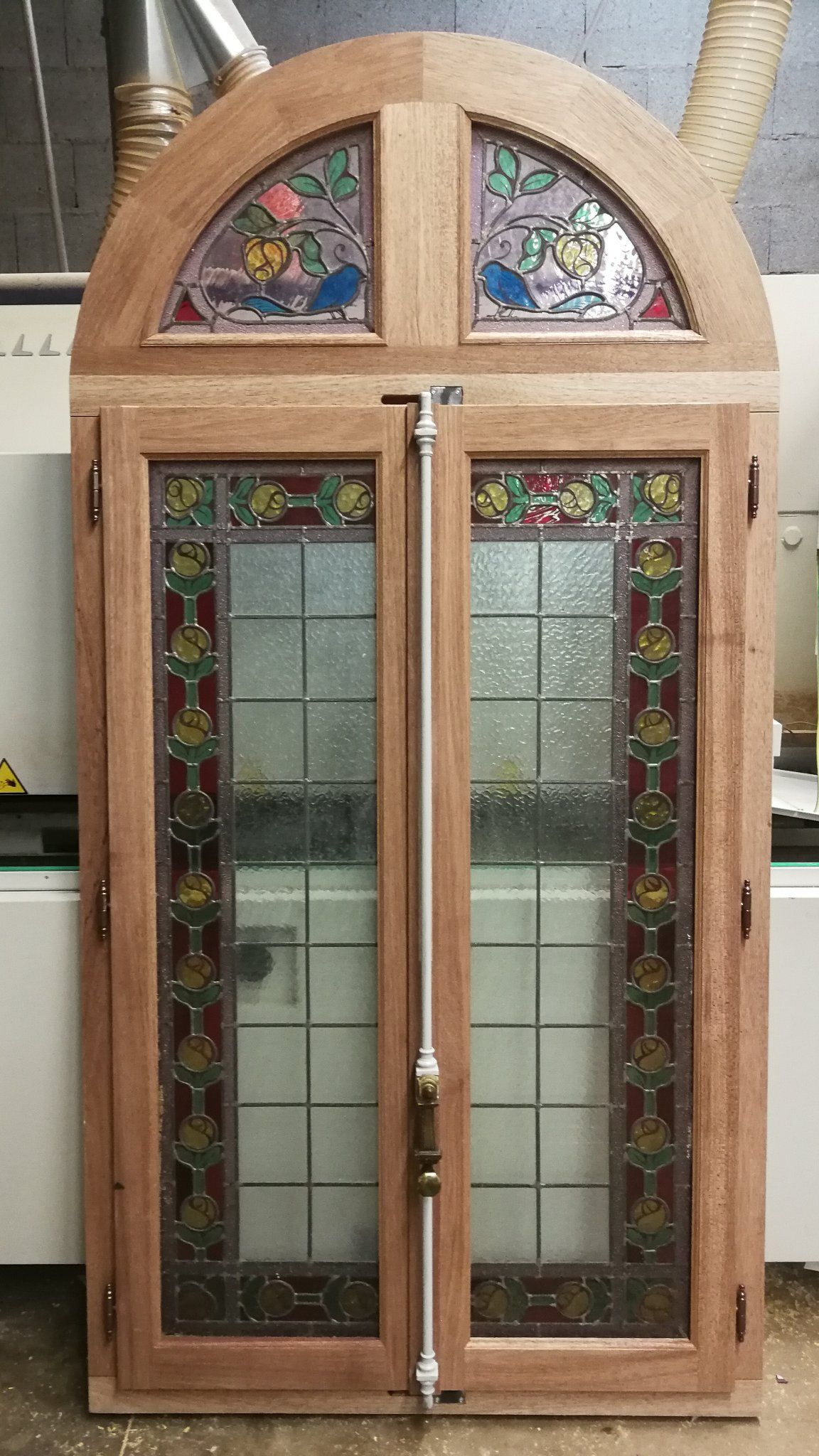 Porte en bois avec panneaux de vitraux et partie supérieure cintrée.