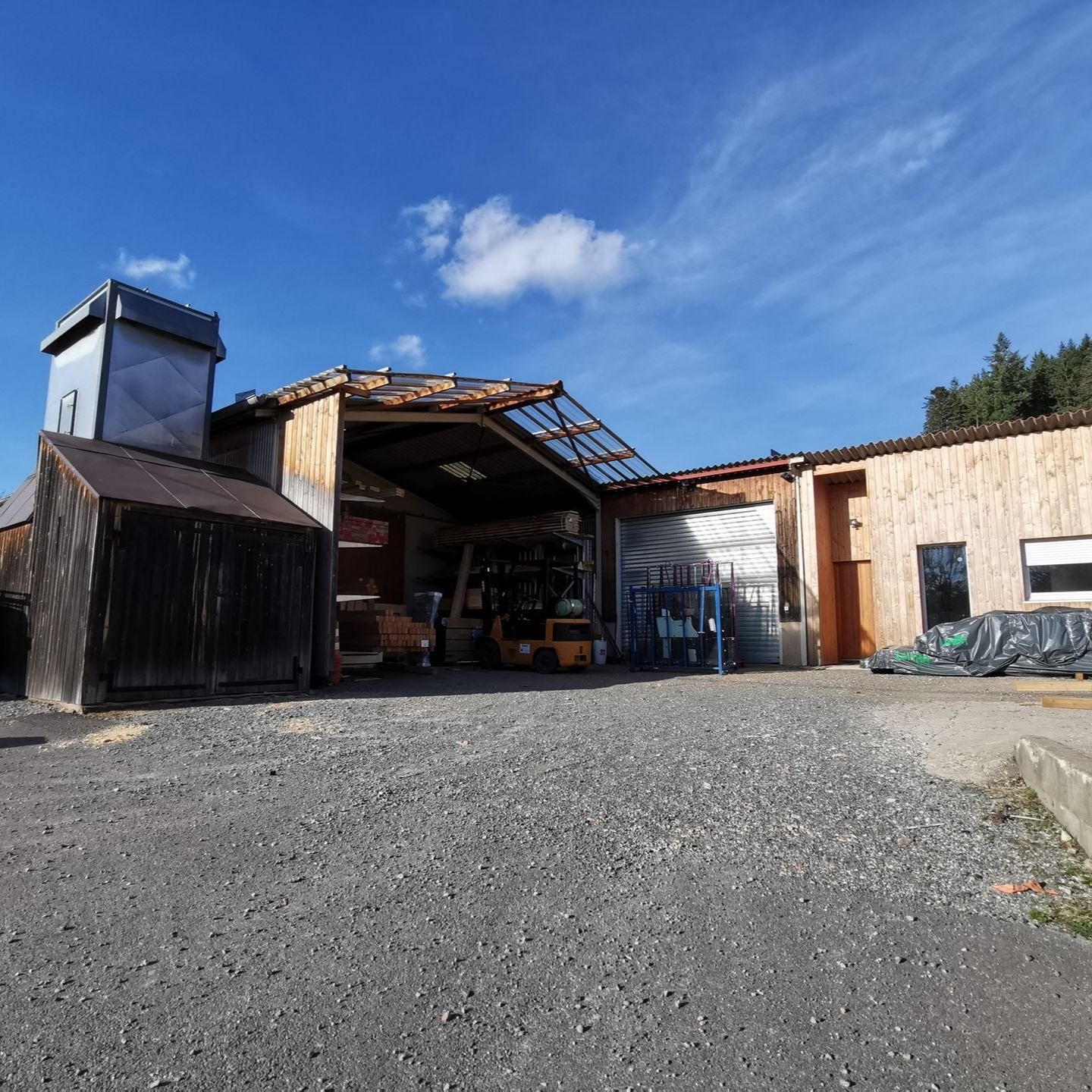 Extérieur de l'atelier de Lombard Menuiserie avec une cour gravillonnée.