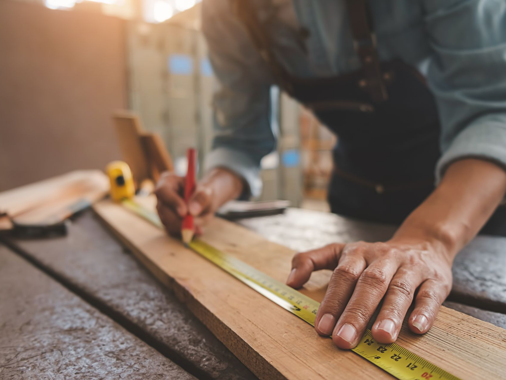 Une personne mesure et marque du bois avec une règle et un crayon sur un établi dans un atelier.