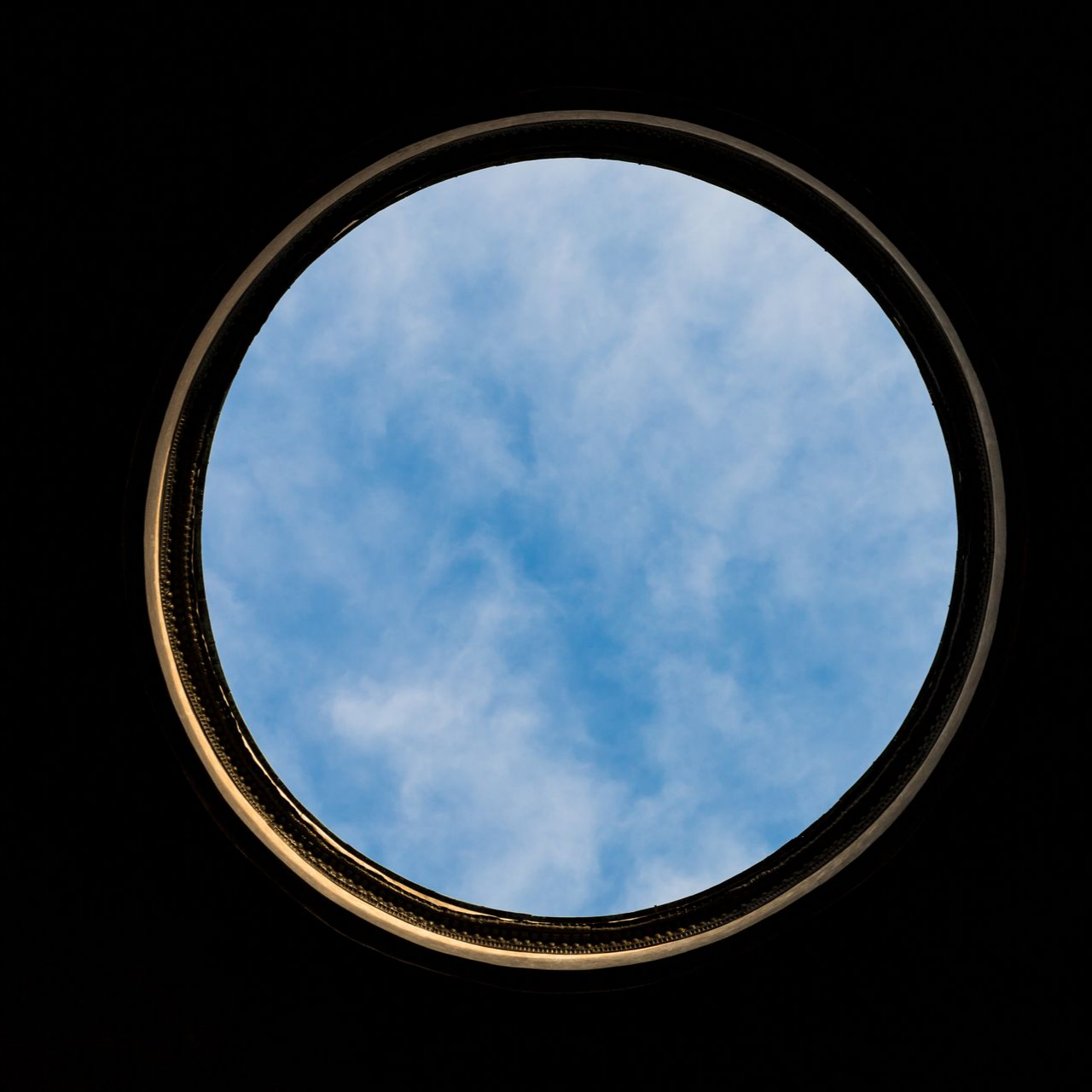 Fenêtre ronde avec vue sur un ciel bleu et des nuages ​​blancs.