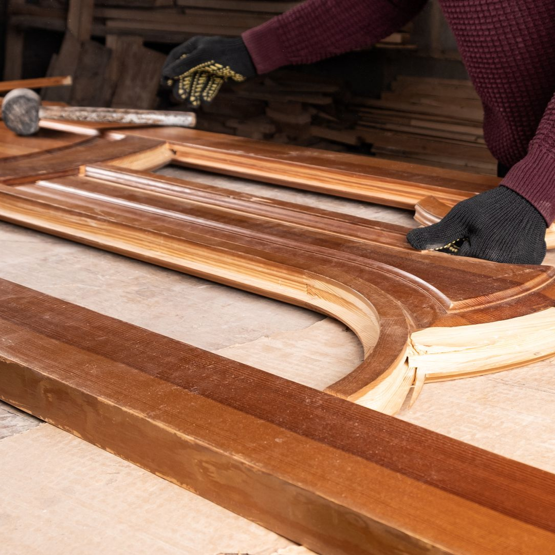Une personne portant des gants travaille sur un cadre en bois, en appliquant une finition.