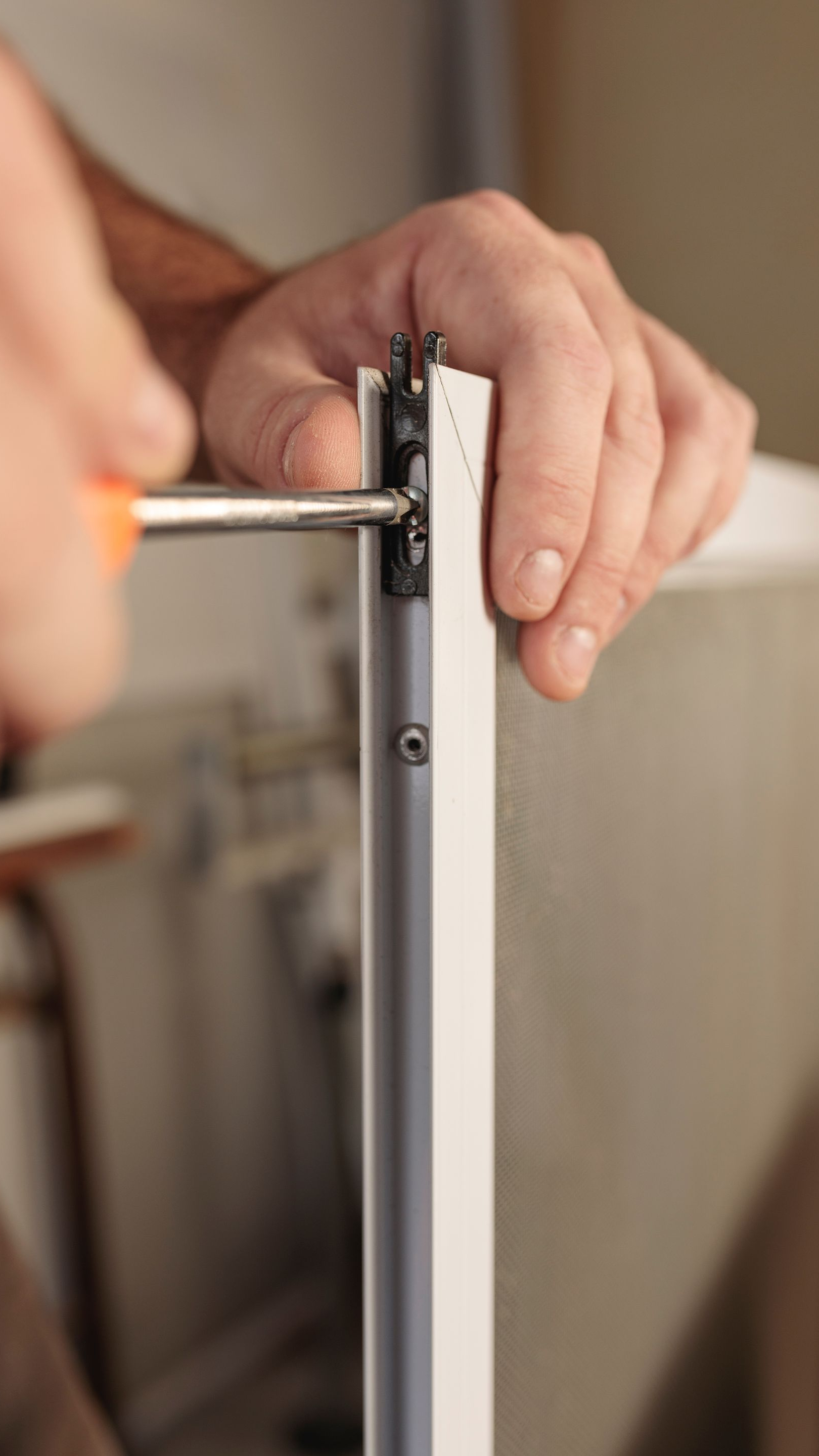 Une personne utilise un tournevis pour serrer une vis sur un cadre blanc.